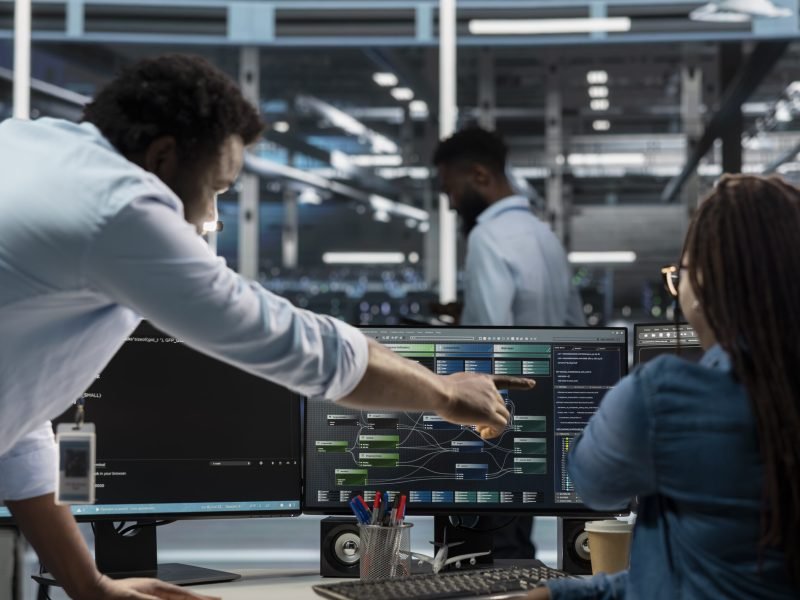 Data center supervisor overseeing admin using PC to visualize artificial intelligence neural networks node trees. Server room manager providing feedback to employee working to oversee AI systems